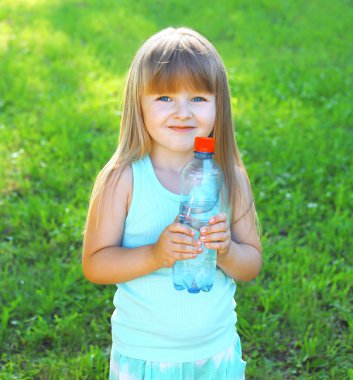 Happpy smiling child and plastic bottle with water on the grass 