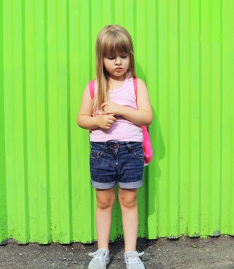 Little girl child with backpack against the colorful green wall