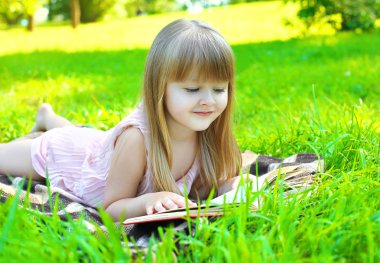 Portrait of little smiling girl child reading a book lying on th