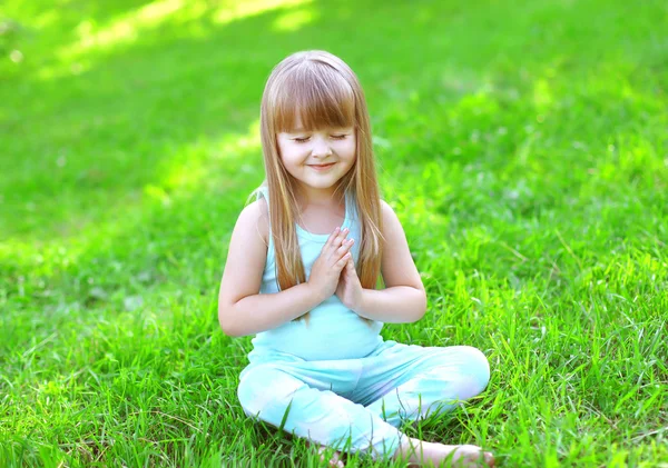 Child doing yoga exercises sitting on the grass in sunny summer — Stok fotoğraf