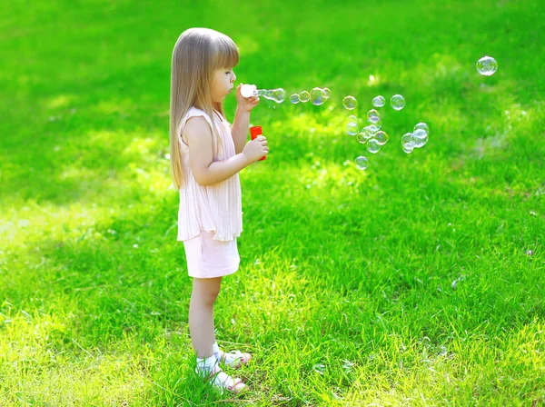 Child standing on the grass blowing soap bubbles in summer day