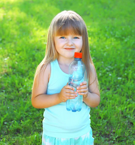 Happpy smiling child and plastic bottle with water on the grass 