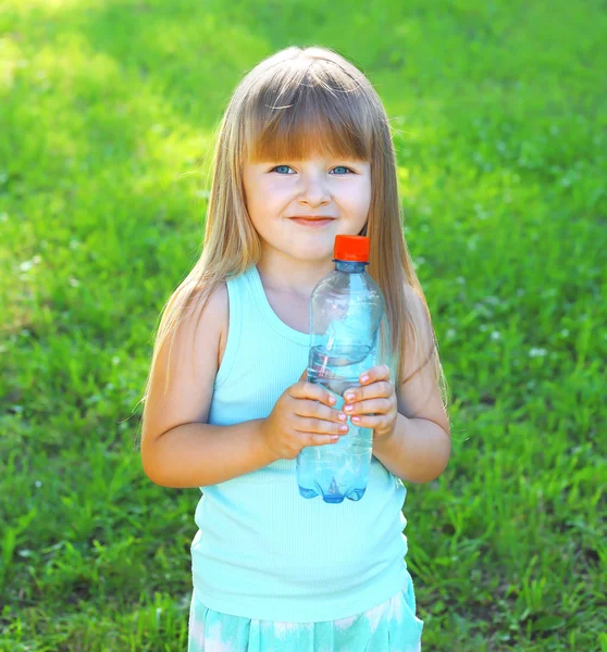 Happpy smiling child and plastic bottle with water on the grass — Stok fotoğraf