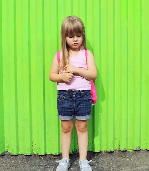 Little girl child with backpack against the colorful green wall — Stok fotoğraf
