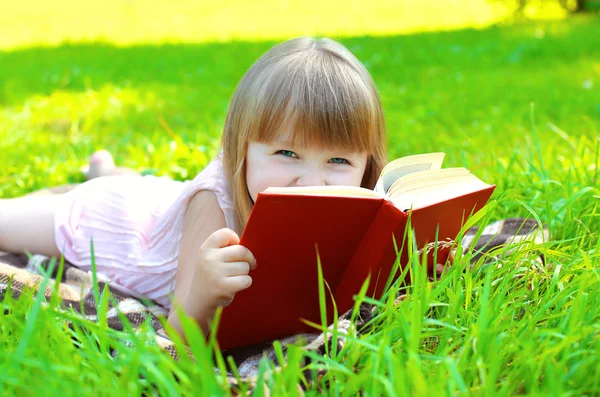 Porträt eines kleinen lächelnden Mädchens mit Buch auf dem Gras liegend — Stockfoto