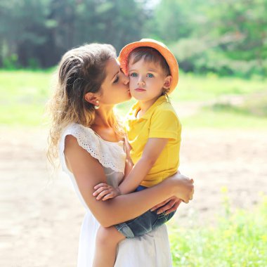 Mother kissing child outdoors in sunny summer day