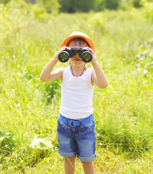 Child boy looks in binoculars outdoors in summer day — Stockfoto