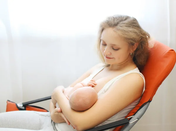 Mãe feliz segurando em mãos bebê e amamentando o peito em casa — Fotografia de Stock