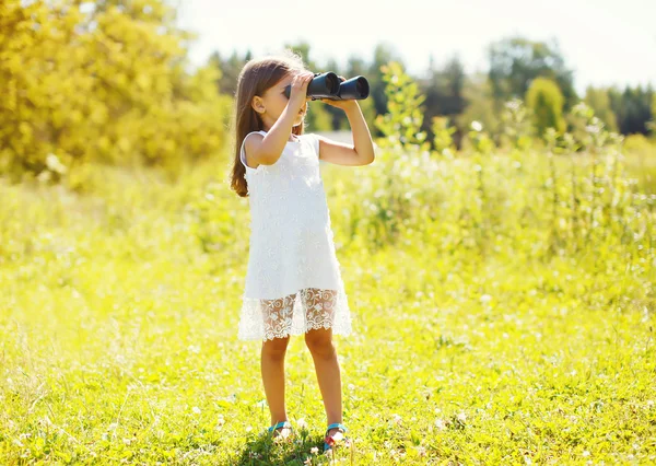 Little girl looks in binoculars outdoors in summer day — Stock Photo, Image