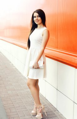 Beautiful young woman in white dress with handbag clutch outdoor