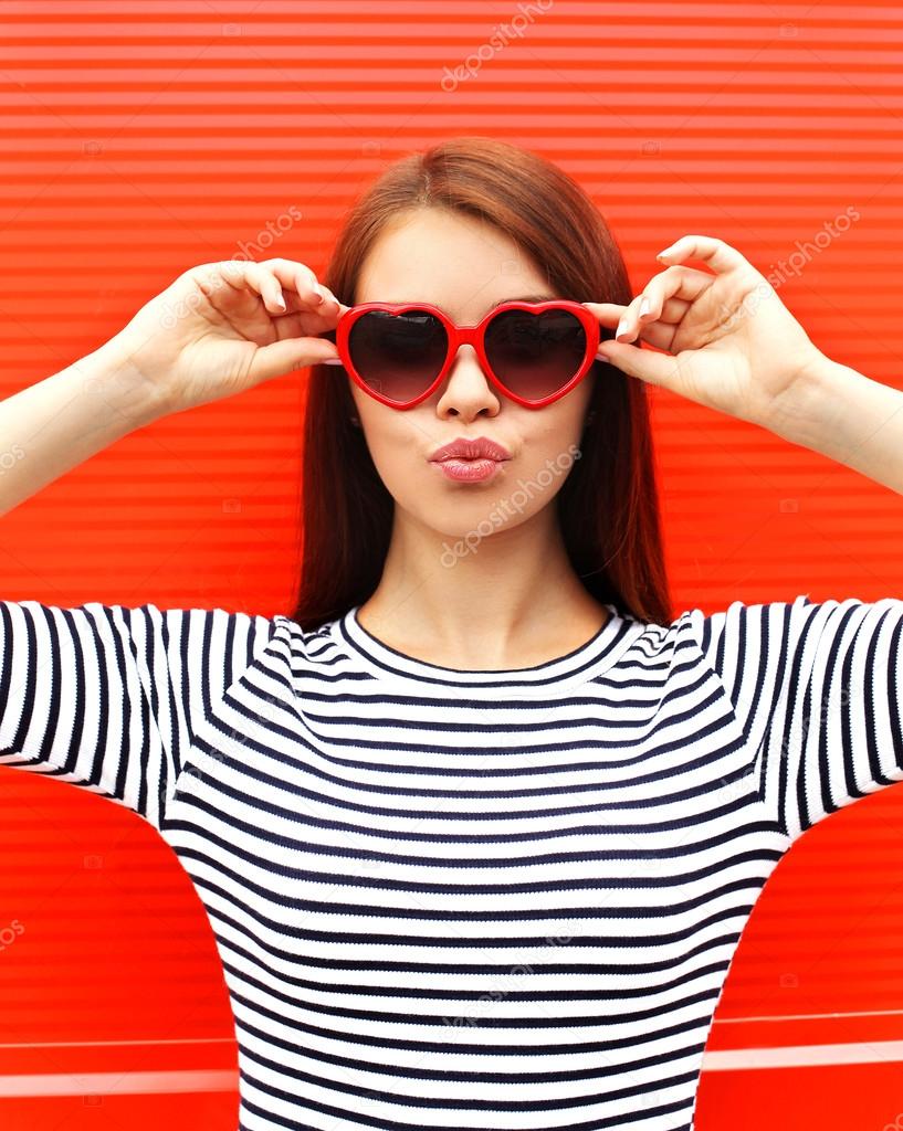 Portrait of pretty young woman in red sunglasses blowing lips ha