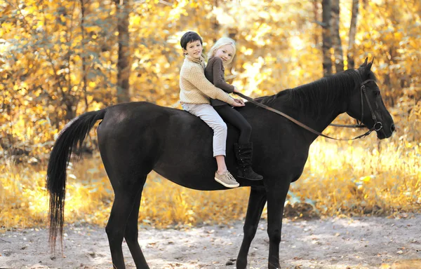 Two children boy and girl riding on horse in autumn forest