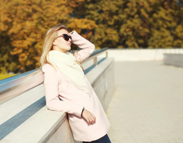 Belle femme blonde portant un manteau rose avec des lunettes de soleil au — Photo