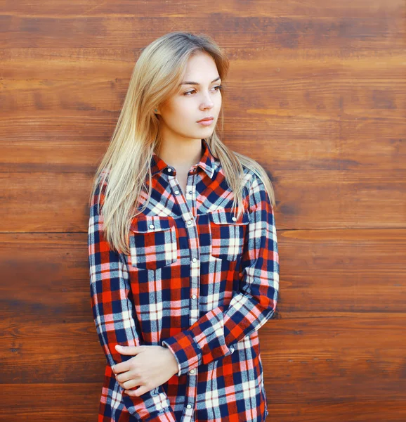 Ziemlich coole blonde Frau im karierten Hemd über braunem Holzbalken — Stockfoto
