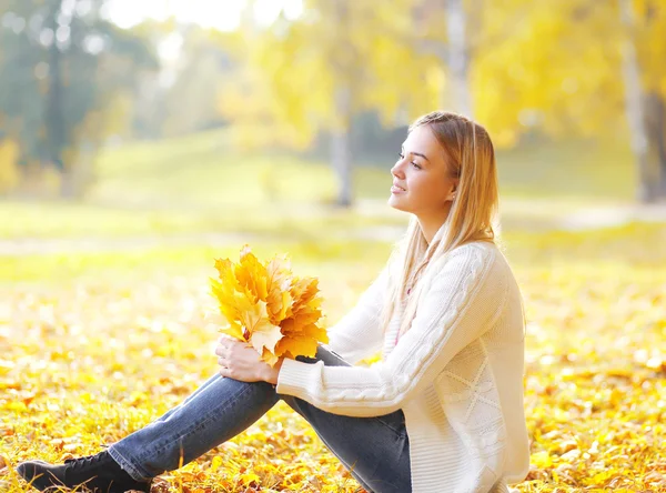 Hübsche junge Frau sitzt mit gelben Ahornblättern im sonnigen Autu — Stockfoto