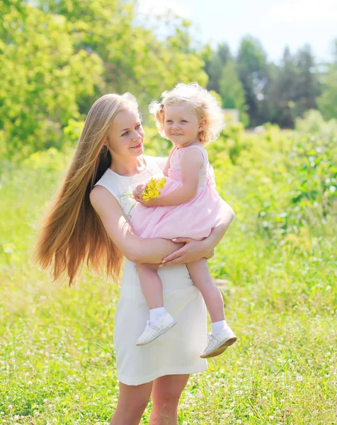 Krásná matka drží v rukou dítěte s květy v létě d — Stock fotografie