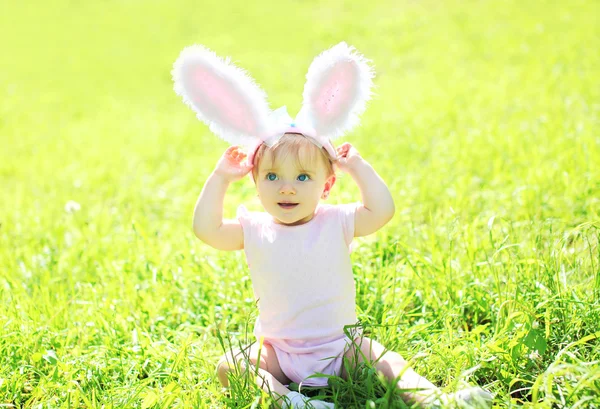 Gelukkig baby met konijn oren zittend op het gras in zonnige zomerdag — Stockfoto