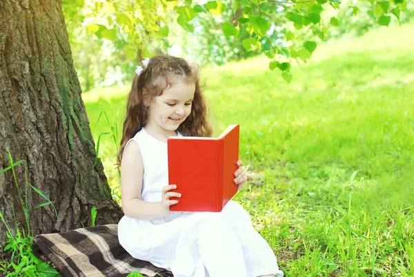 Happy child reading book on grass in summer park — Stock Photo, Image