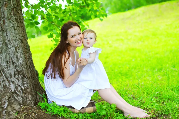 Gelukkig moeder en kind zittend op het gras onder boom in de zomer — Stockfoto