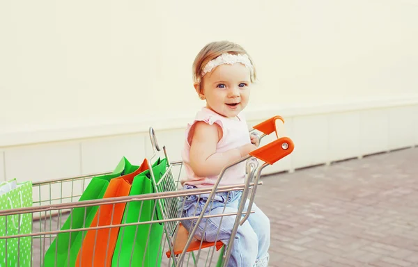 Щаслива усміхнена дитина сидить у візку з барвистим покупцем — стокове фото
