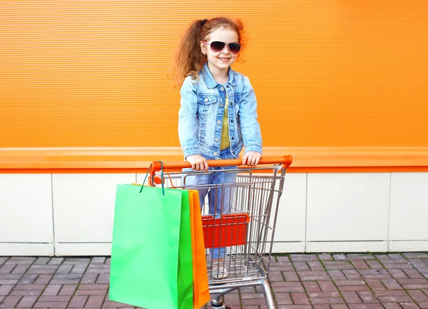 Happy smiling little girl child in trolley cart with colorful sh — Stock Photo, Image