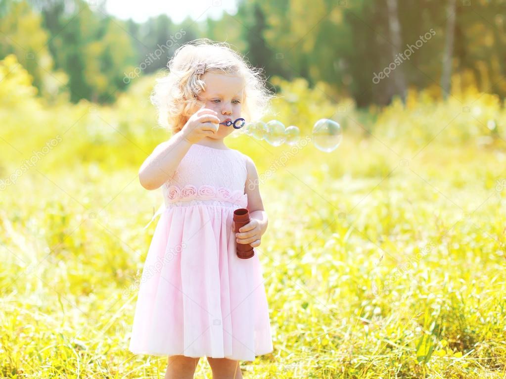 Little girl child blowing soap bubbles in sunny summer day