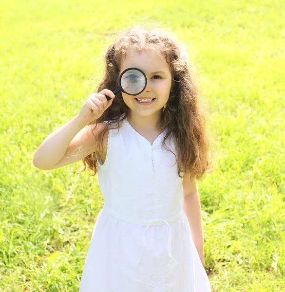 Little girl child looking through a magnifying glass on nature s — Stock Photo, Image