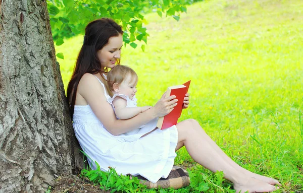 Mãe e criança lendo livro juntos sob a árvore no parque de verão — Fotografia de Stock