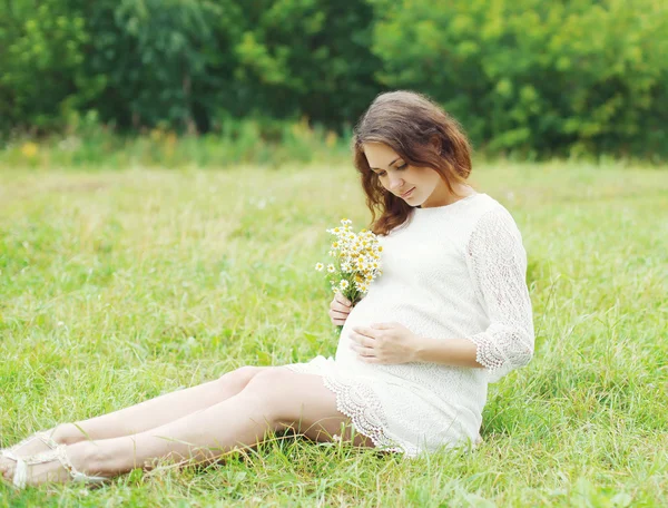 Beautiful young pregnant woman with chamomiles flowers lying on — Stok fotoğraf