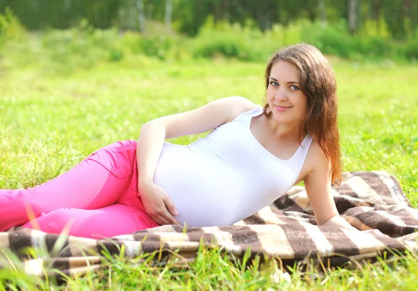 Happy smiling pregnant woman resting lying on grass in summer da — Stok fotoğraf