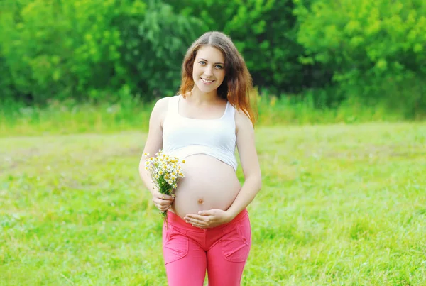 Happy smiling young pregnant woman with flowers outdoors in summ — 图库照片