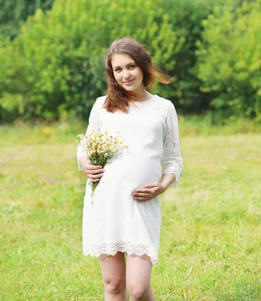 Feliz joven embarazada con flores de manzanillas al aire libre —  Fotos de Stock