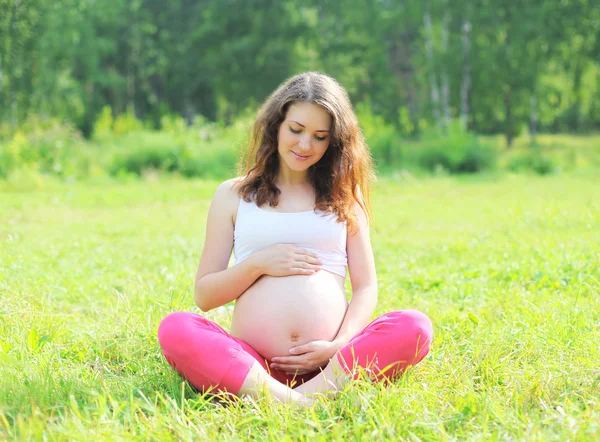 Happy young pregnant woman sitting on grass doing yoga — Stock Photo, Image