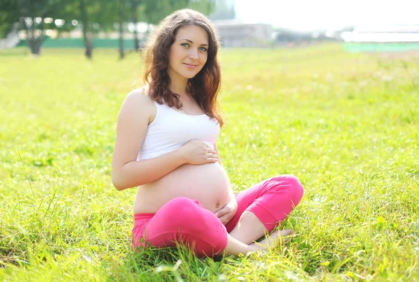 Heureuse jeune femme enceinte assise sur l'herbe faisant du yoga sous le soleil — Photo