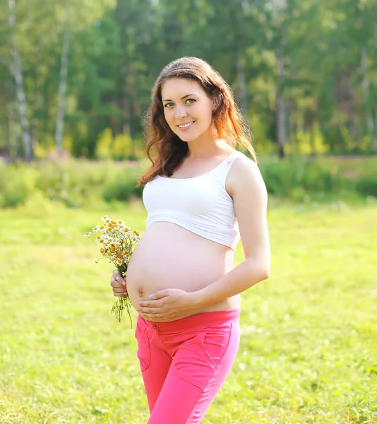 Happy young pregnant woman with flowers outdoors in summer day — Stock Photo, Image