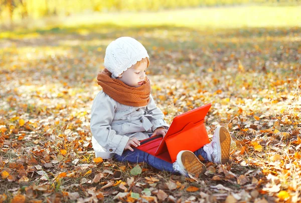 Little child sitting using tablet pc in autumn park — Stock Photo, Image