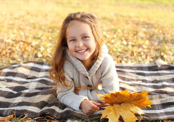 Portrait of happy smiling child lying on plaid with yellow maple — Stock Photo, Image