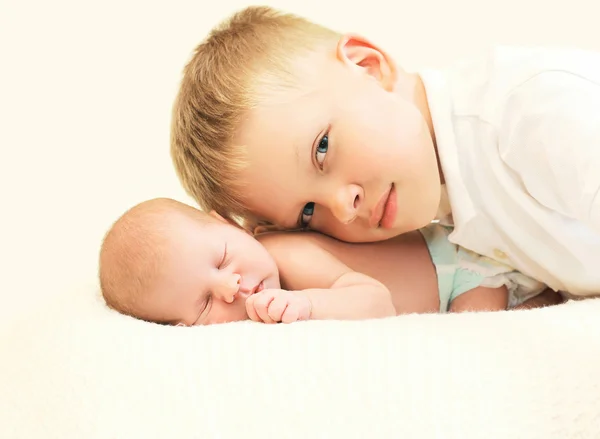 Two children lying on bed, eldest brother hugging youngest baby — Stock Photo, Image