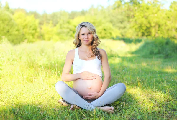 Feliz sonriente joven embarazada sentada en la hierba haciendo yoga i —  Fotos de Stock
