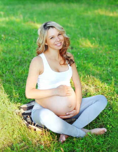 Portrét šťastný usměvavá mladá těhotná žena sedící na trávě doi — Stock fotografie