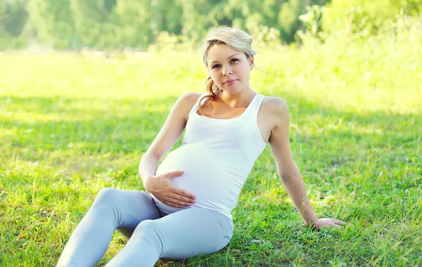 Young pregnant woman sitting on grass in summer sunny day — Stock Photo, Image