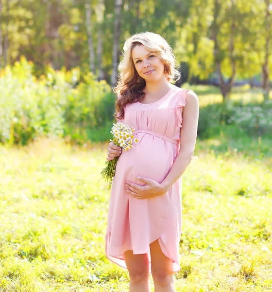 Jeune femme enceinte avec des fleurs de camomille en plein air en été — Photo