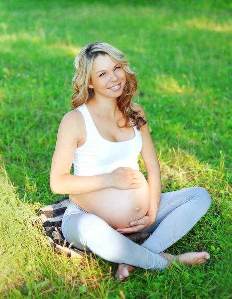 Portrait happy smiling young pregnant woman sitting on grass doi Stock Picture