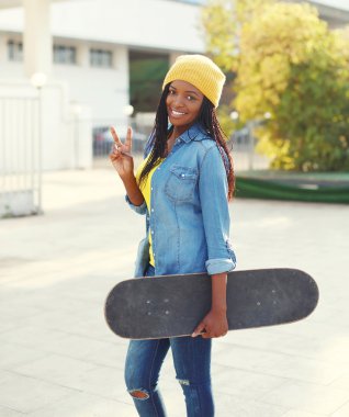 Pretty cool smiling young african woman with skateboard in color