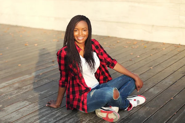 Beautiful young smiling african woman sitting in city evening — Stockfoto