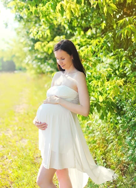 Jovem mulher grávida bonita em vestido branco na natureza em ensolarado — Fotografia de Stock