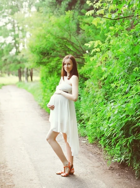 Krásná mladá těhotná žena v bílých šatech venku v přírodě — Stock fotografie