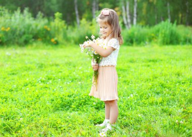 Cute smiling child with bouquet chamomiles flowers in summer day