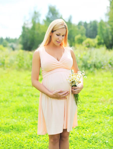Beautiful young pregnant woman with chamomiles flowers in sunny — Stockfoto