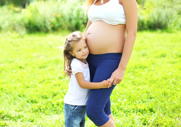 Mulher grávida feliz, criança pequena filha escuta barriga mãe — Fotografia de Stock